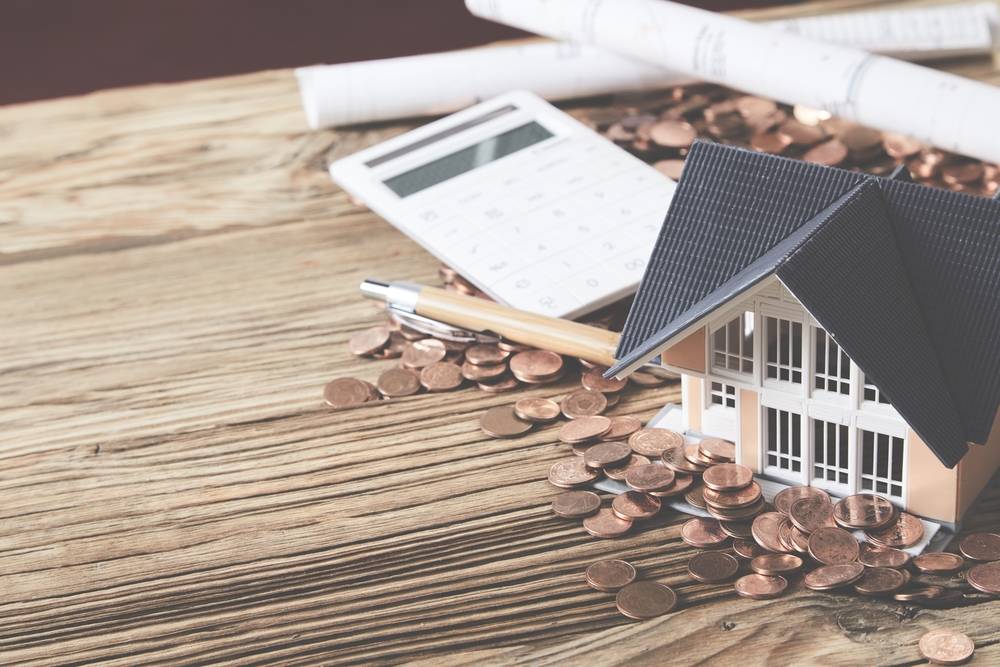 home plans, a calculator, a pile of pennies, and a model of a house