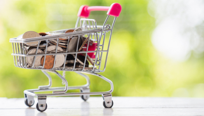 A lot of coins in pink mini shopping cart on white wooden table with nature background