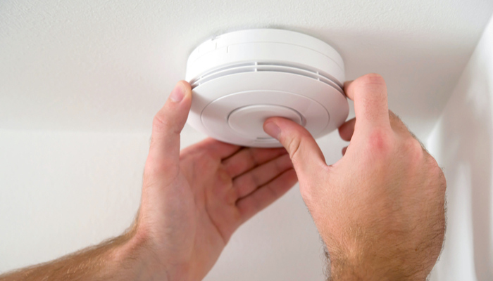 Man installing smoke or carbon monoxide detector on a white ceiling