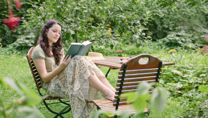 A woman in green shirt and long skirt sitting in the garden reading a book