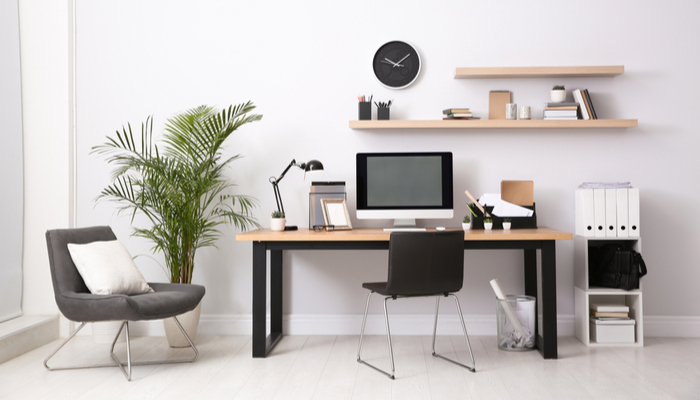 Modern mac computer and office supplies on table with black chairs in office interior