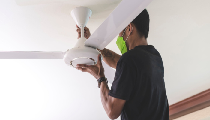 A handyman in black shirt installs a ceiling fan, tightening the screws of the fan blades