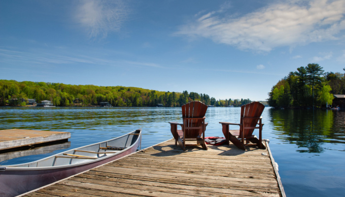 Sunrise on two empty chairs sitting on a dock on a lake with boat on the side