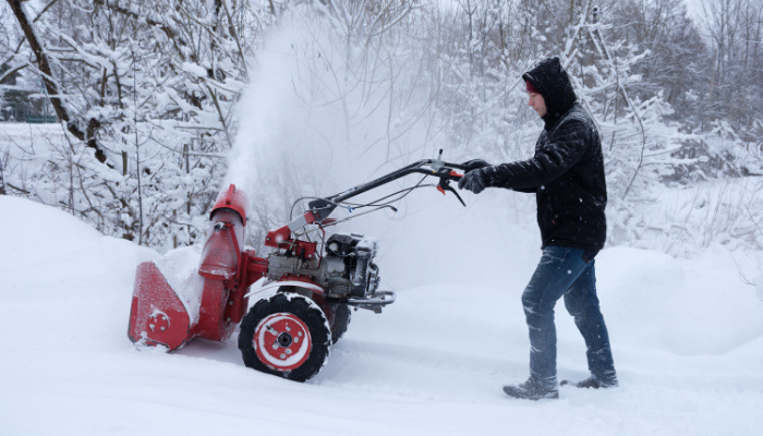 young man on a black jacket clearing snow in backyard with wheeled snow blower