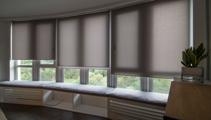 Automatic roller blinds beige color on big glass windows with green trees outside
