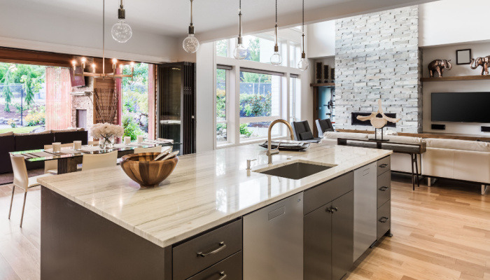 Modern Kitchen with Large Island, Sink, Cabinets, and Hardwood Floors in New Luxury Home, with View of Living Room and Dining Room