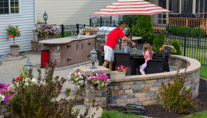 Daddy serving lemonade to his little daughter outdoors on a brick patio with outdoor kitchen and gas barbecue in summer