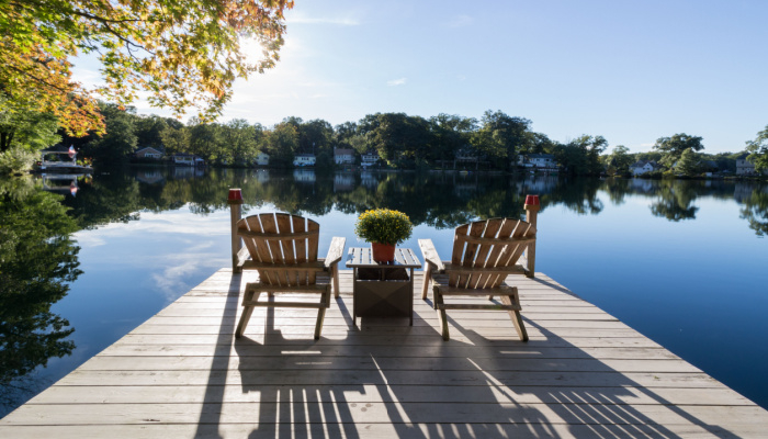 View of dock with chairs and a table with plant on a beautidul pristine lake with reflections and shadows