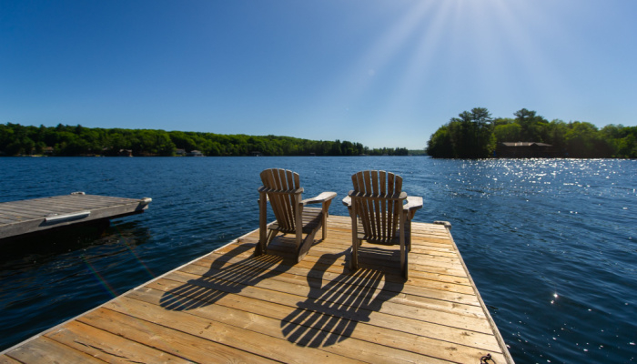 Cottage life - Sunrise on two empty Adirondack chairs sitting on a dock on a the sun light create long shadows on the wooden dock