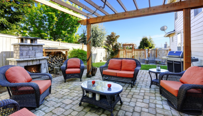 Backyard cozy patio area with wicker furniture set and brick fireplace with pergola