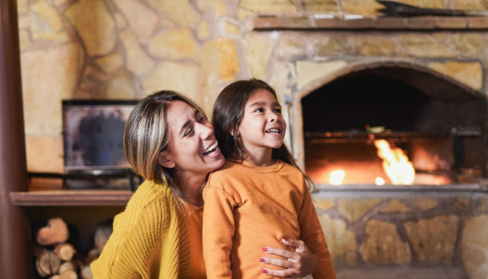 Loving mother hugging little daughter laughing together at home on patio next to the fireplace