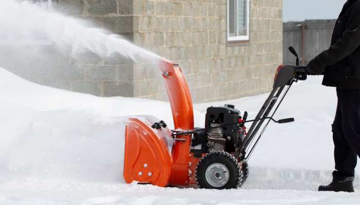 A man removing snow during winter using a portable snow blower powered by gasoline