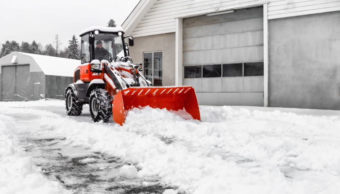 Little red tractor with snowplow in a motion removing snow on a yard of a house