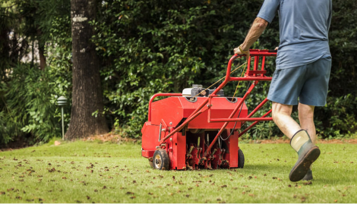 Man in boots using gas powered aerating machine to aerate residential grass yard