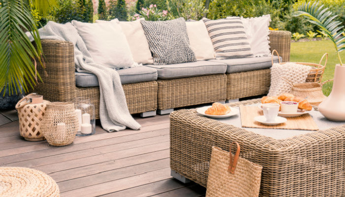 beautiful Wicker patio set with beige cushions standing on a wooden board deck with plants on the background