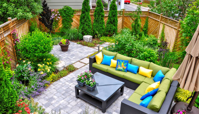 A beautiful urban backyard garden featuring a tumbled paver patio, with furnitures, flagstone stepping stones, and a variety of trees, shrubs and perennials add colour and year round interest