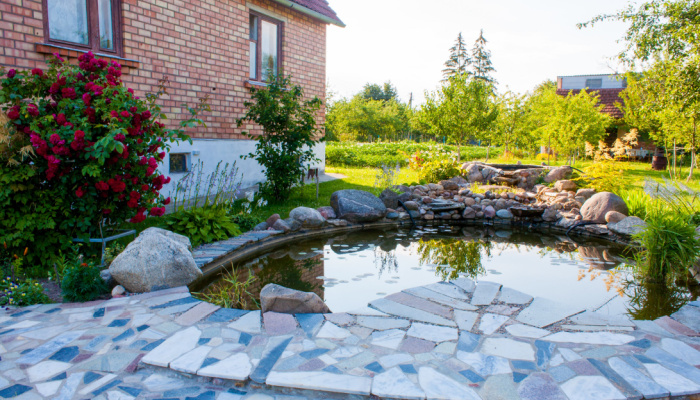 Beautiful pond in a large backyard of a red brick home surrounded with stone during spring