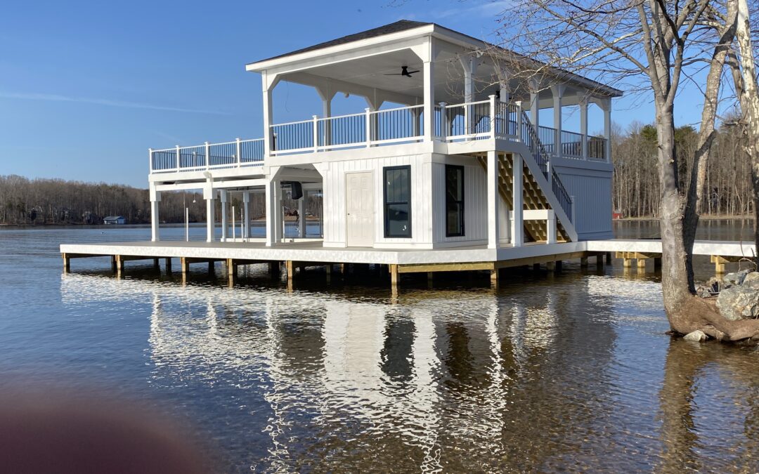 Custom-built wooden boathouse with gabled roof, dual boat lifts, and wide dock extending over clear lake water — Sacra Custom Homes